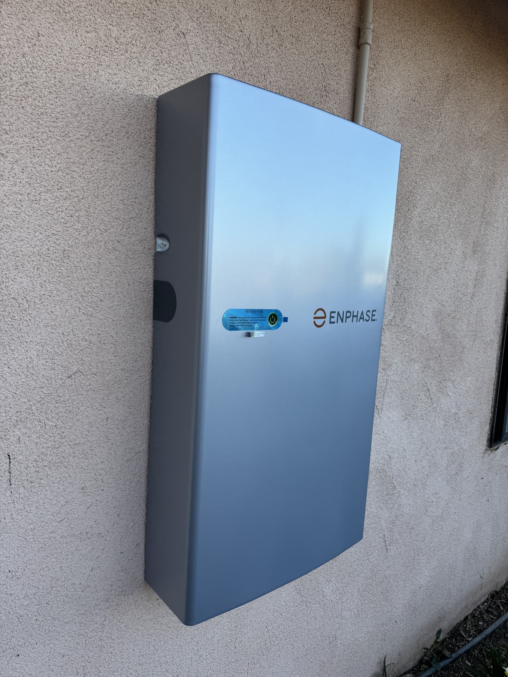 Completed wall-mounted home battery storage unit installed beside its electrical disconnect, with conduit runs finished
